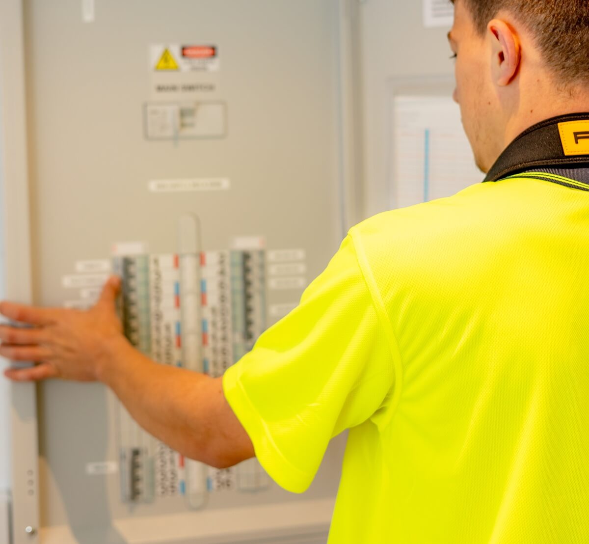 Electrician from PWA Electrical Services in a high-visibility shirt inspecting a commercial-grade electrical switchboard, reviewing clearly labelled circuit breakers and main switch controls