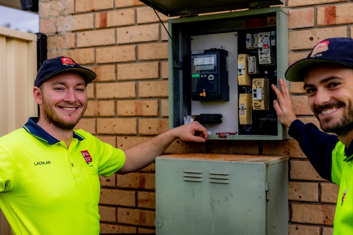 Licensed electricians in PWA Electrical Services uniforms performing a routine electrical check on a residential switchboard with detailed breaker labels and RCD protection