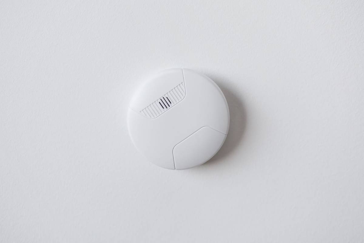 Modern smoke alarm mounted on a white ceiling, photographed close-up from below.