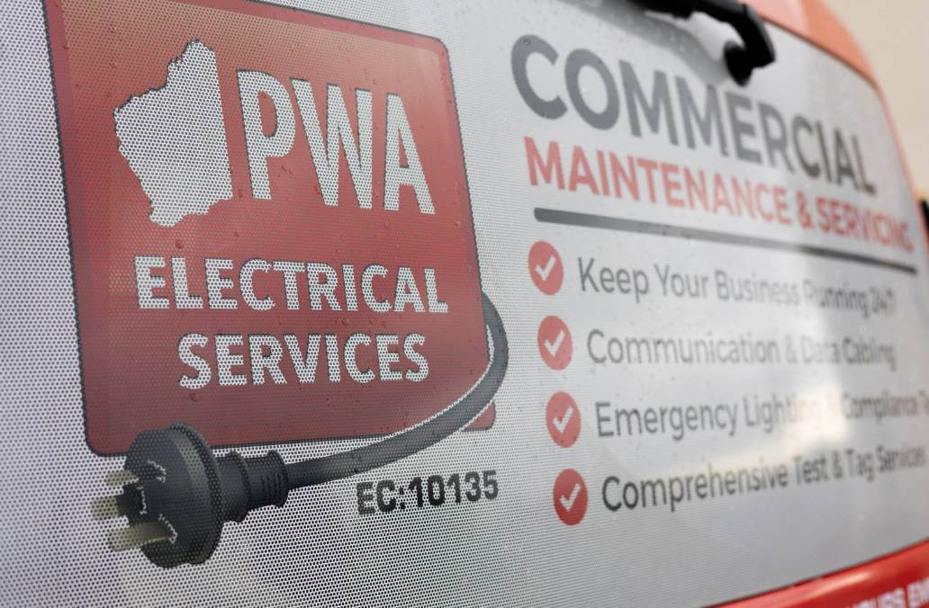 PWA Electrical Services advertisement on a vehicle window, listing commercial maintenance and servicing offerings including 24/7 business support, data cabling, emergency lighting compliance, and test and tag services.