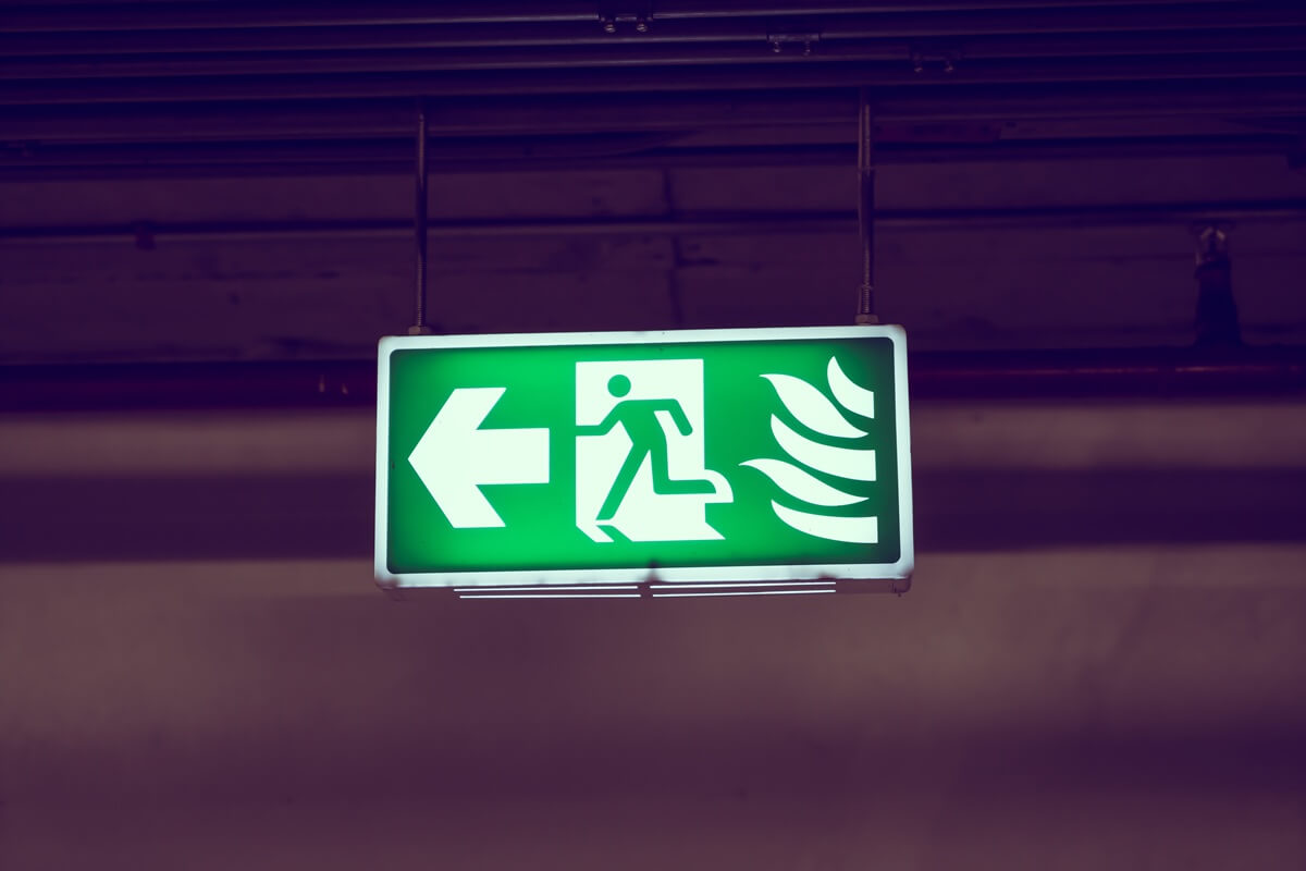 Illuminated green emergency exit sign with a running figure and left arrow, indicating evacuation direction in case of emergency