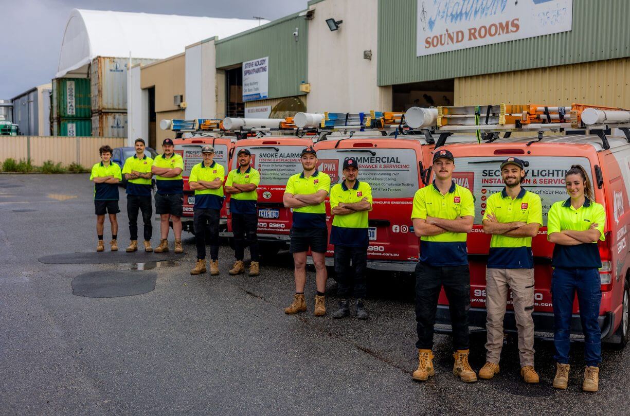 Team of PWA Electrical Services staff standing in front of branded service vehicles outside the company’s warehouse in Perth