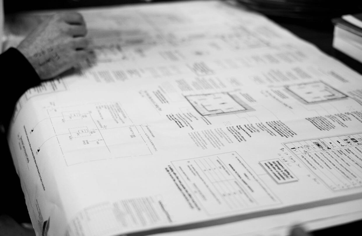 Close-up of technical electrical plans spread across a table, with a person's hand visible above the paper