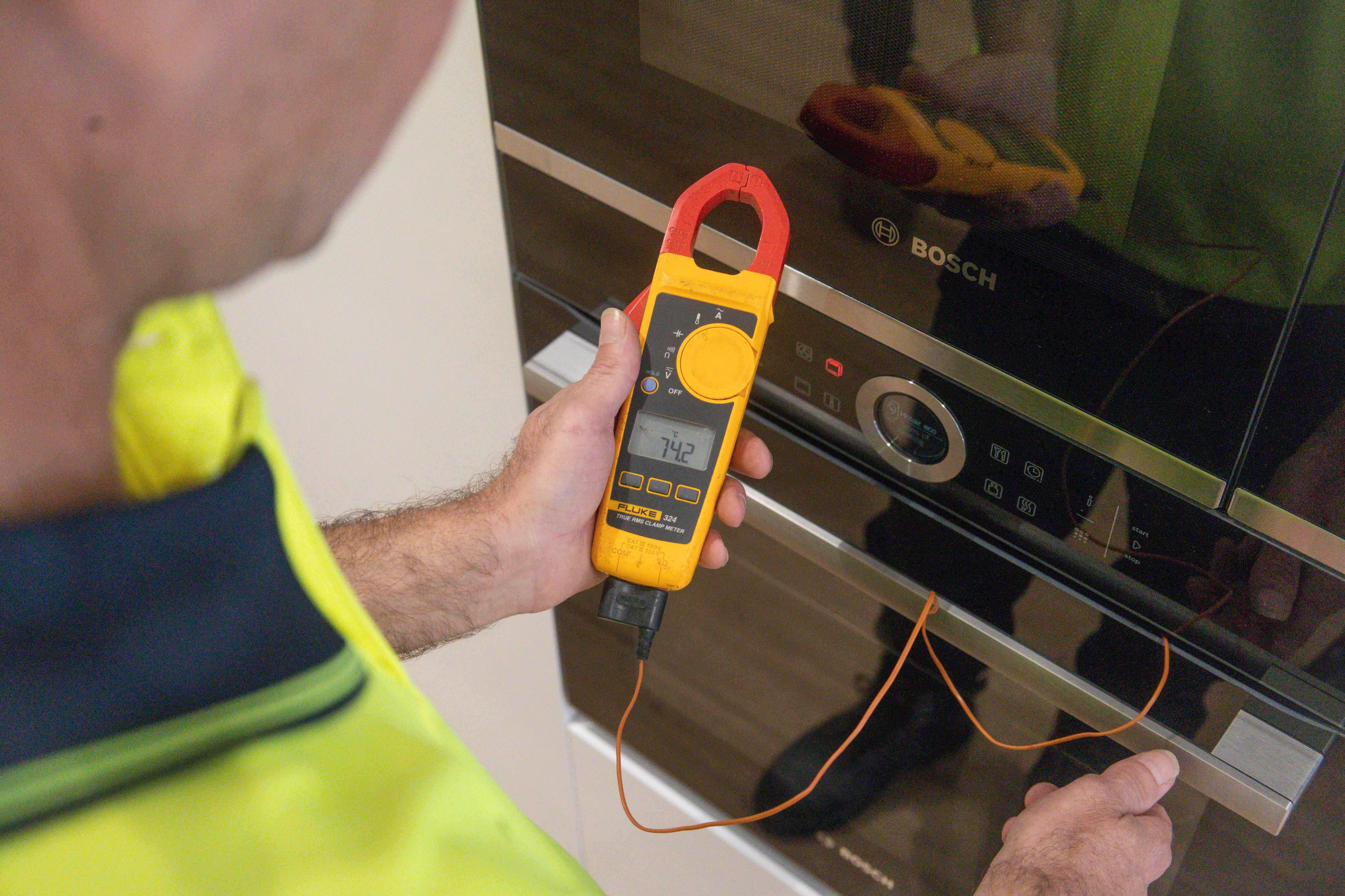 Electrician testing an oven with a clamp meter during electrical fault finding in a residential kitchen in Kalamunda