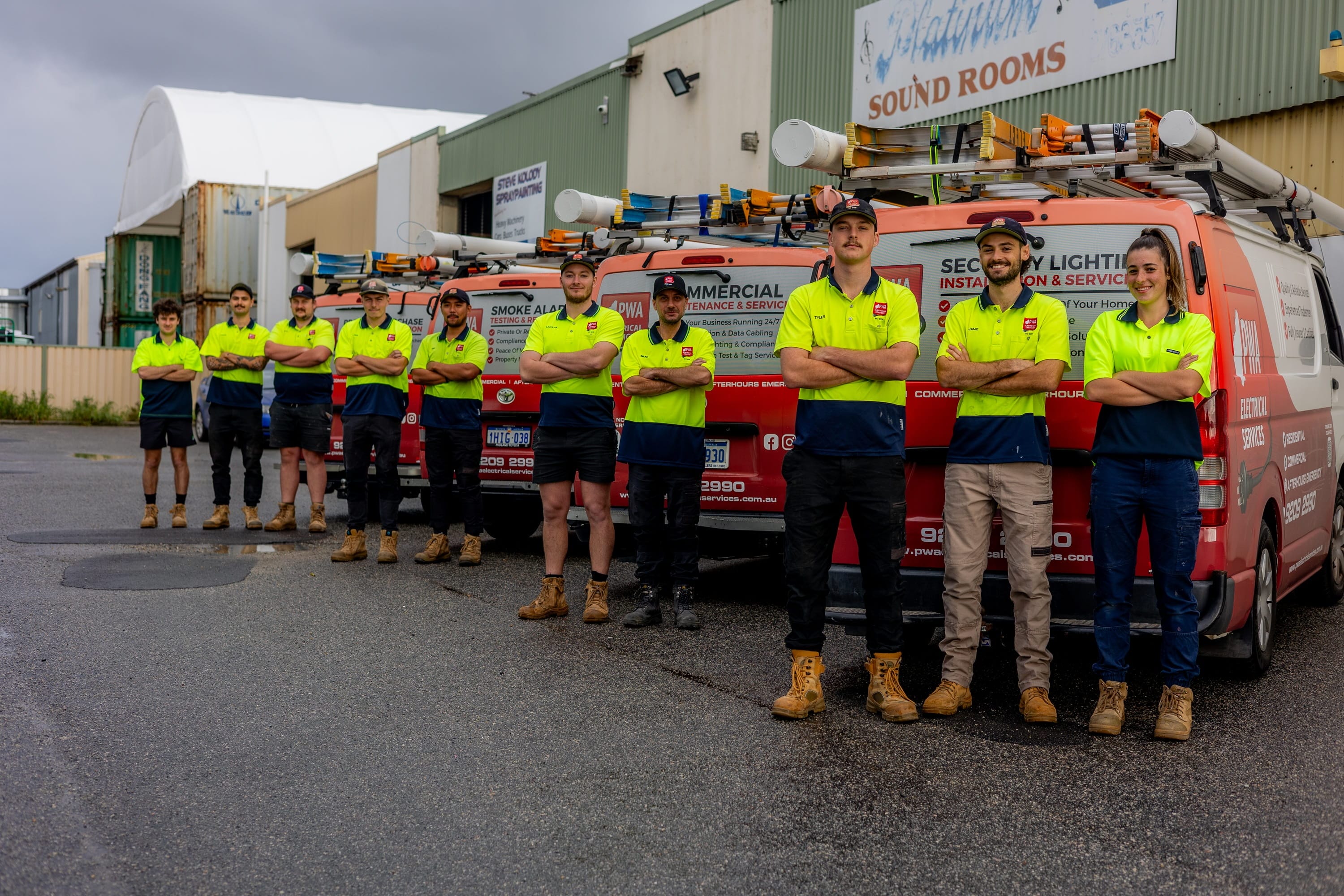 PWA Electrical Services team standing in front of branded service vehicles at a commercial site.