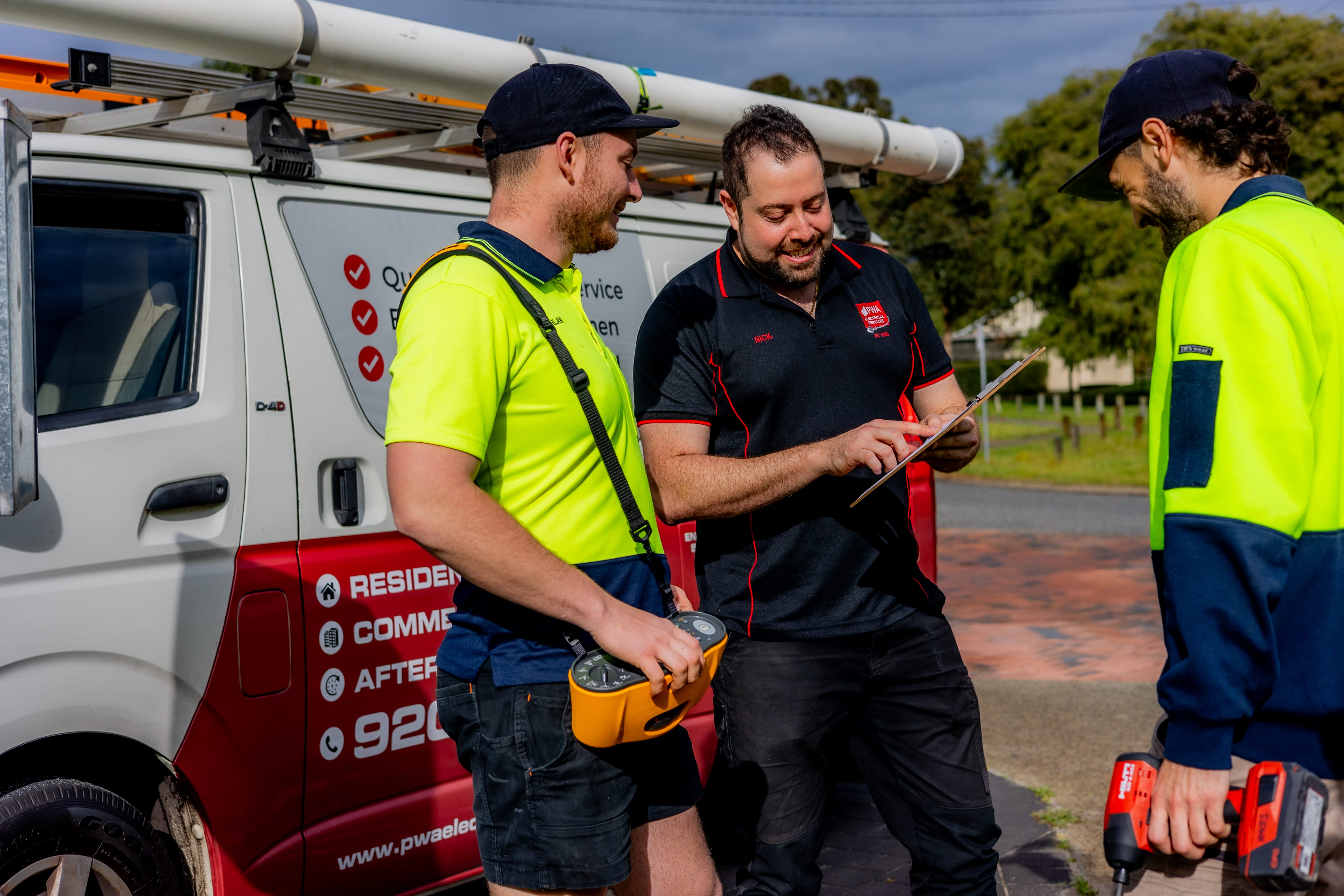 PWA Electrical Services team reviewing job details beside service vehicle in a residential area.