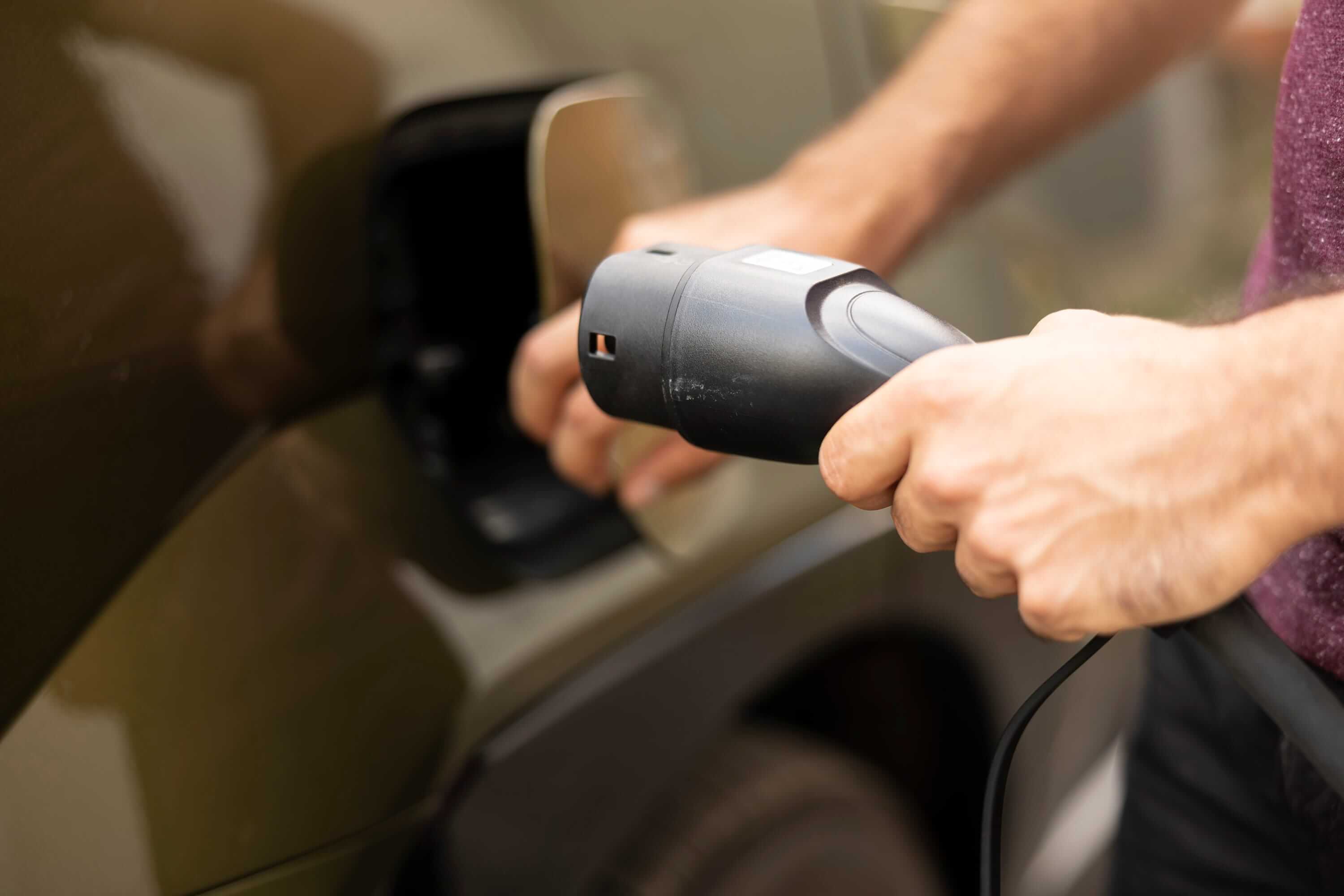 Close-up of a person connecting an electric vehicle charging plug to a car charging port.