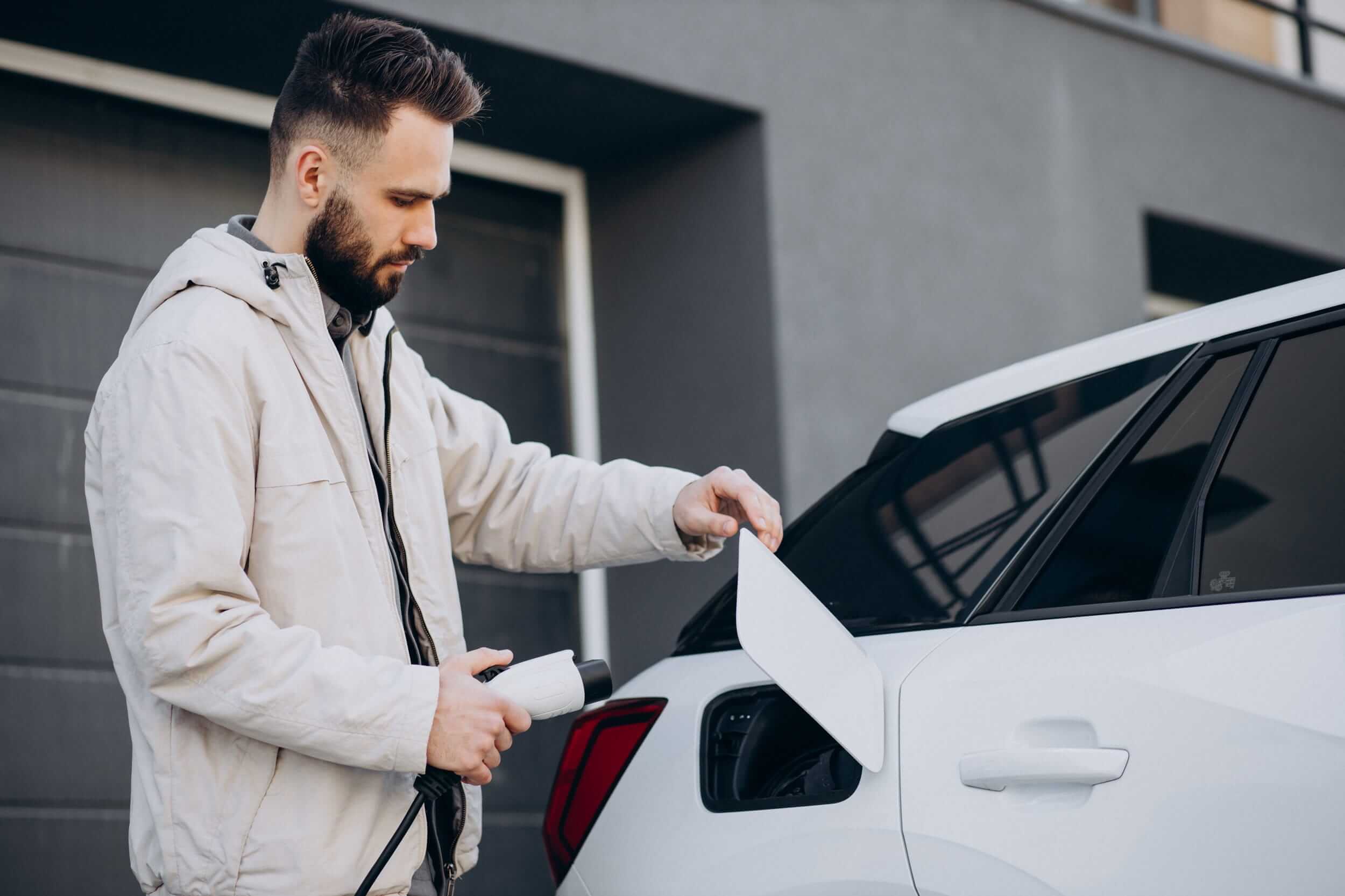 Man plugging an electric vehicle into a home charging point outside a modern house.