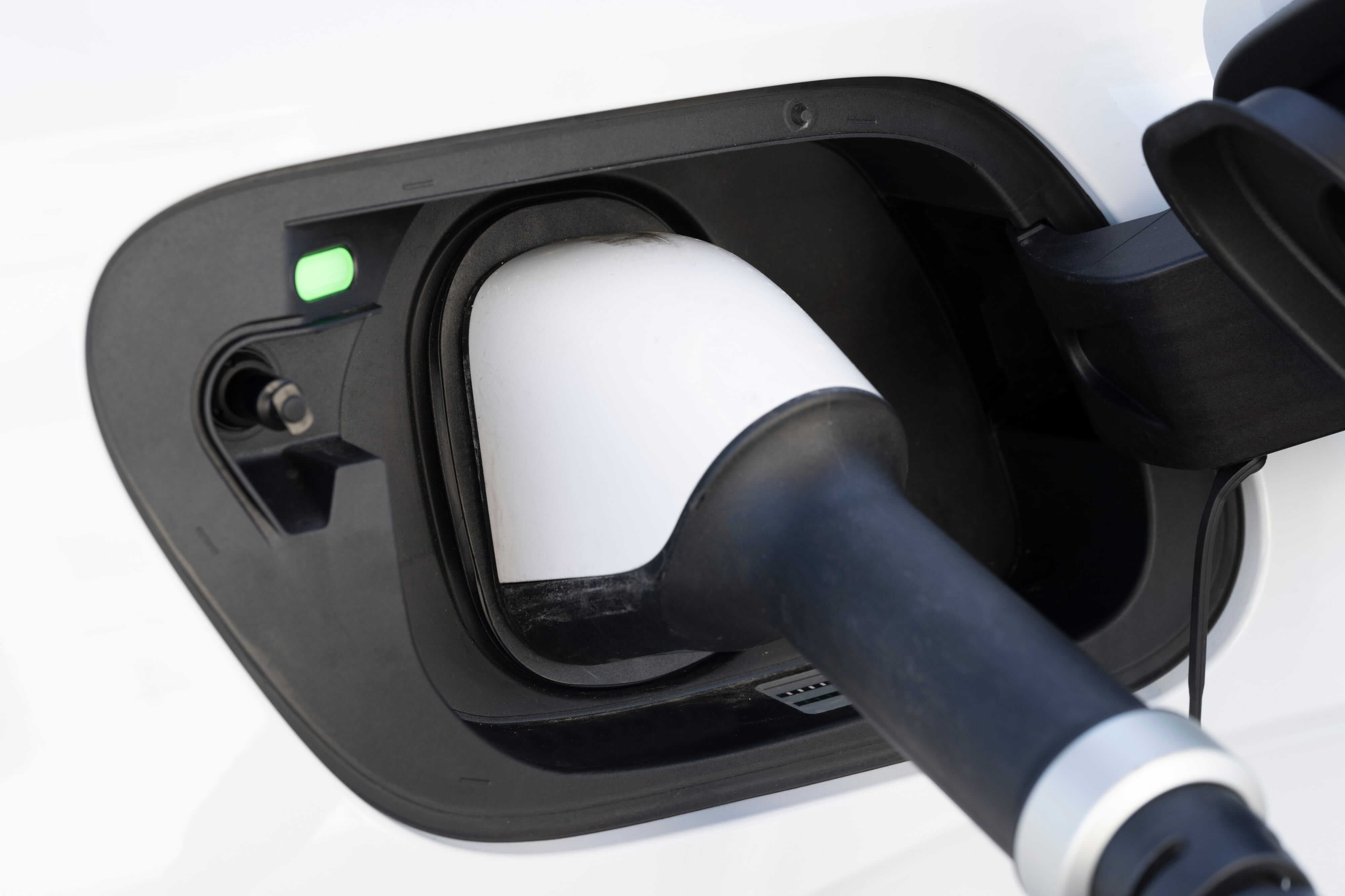 Close-up of an electric vehicle charging port with plug connected and indicator light visible.