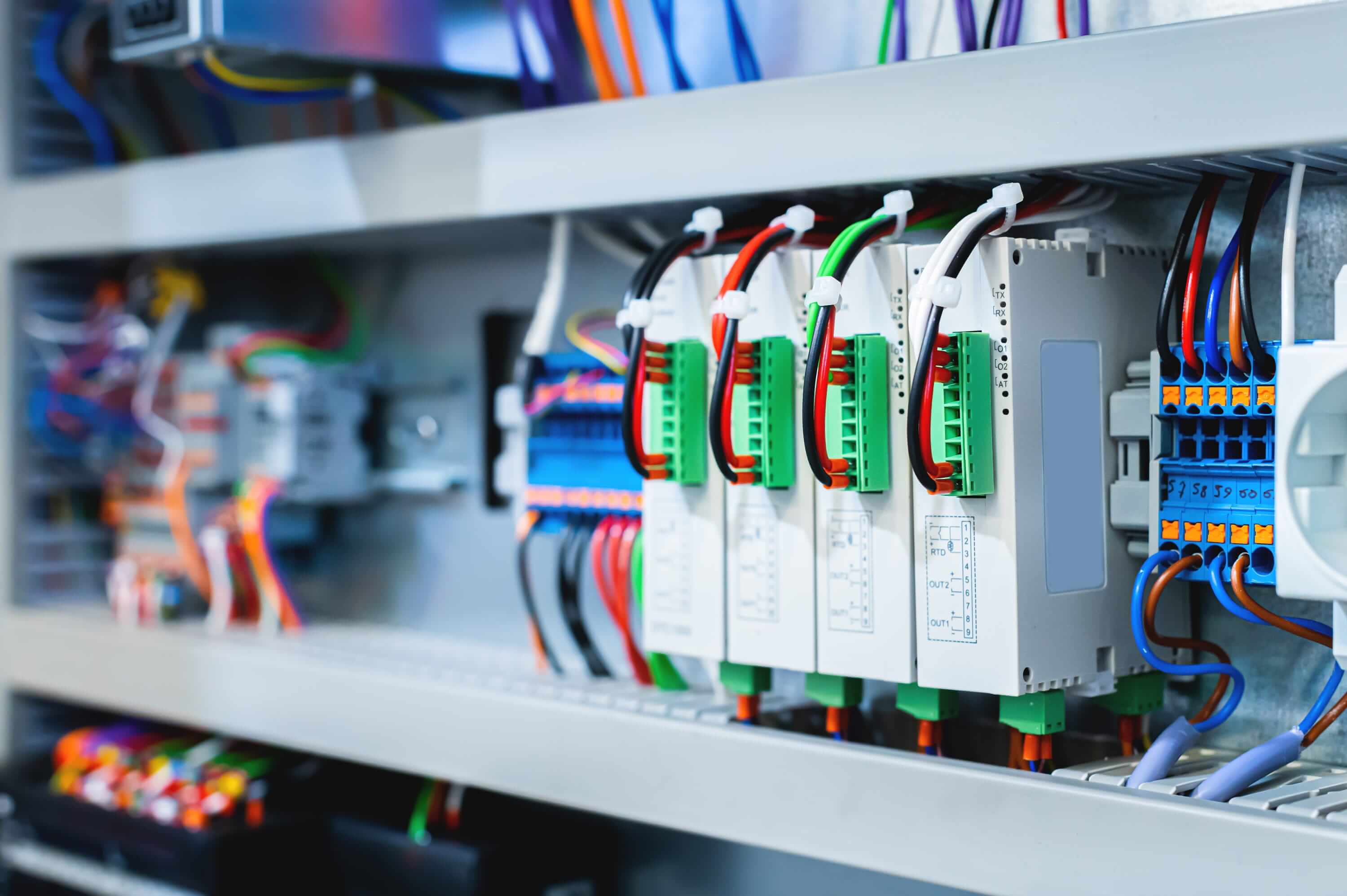 Industrial electrical control cabinet with multiple batch switches, coloured wiring, and inverter modules on a production line.